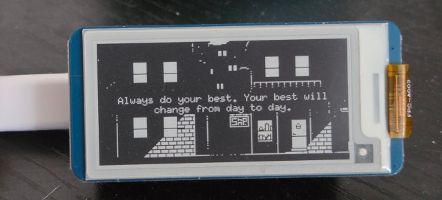 A small e-paper display, showing the words "Always do your best. Your best will change from day to day". The text is superimposed over a 1-bit image of a night-time street.